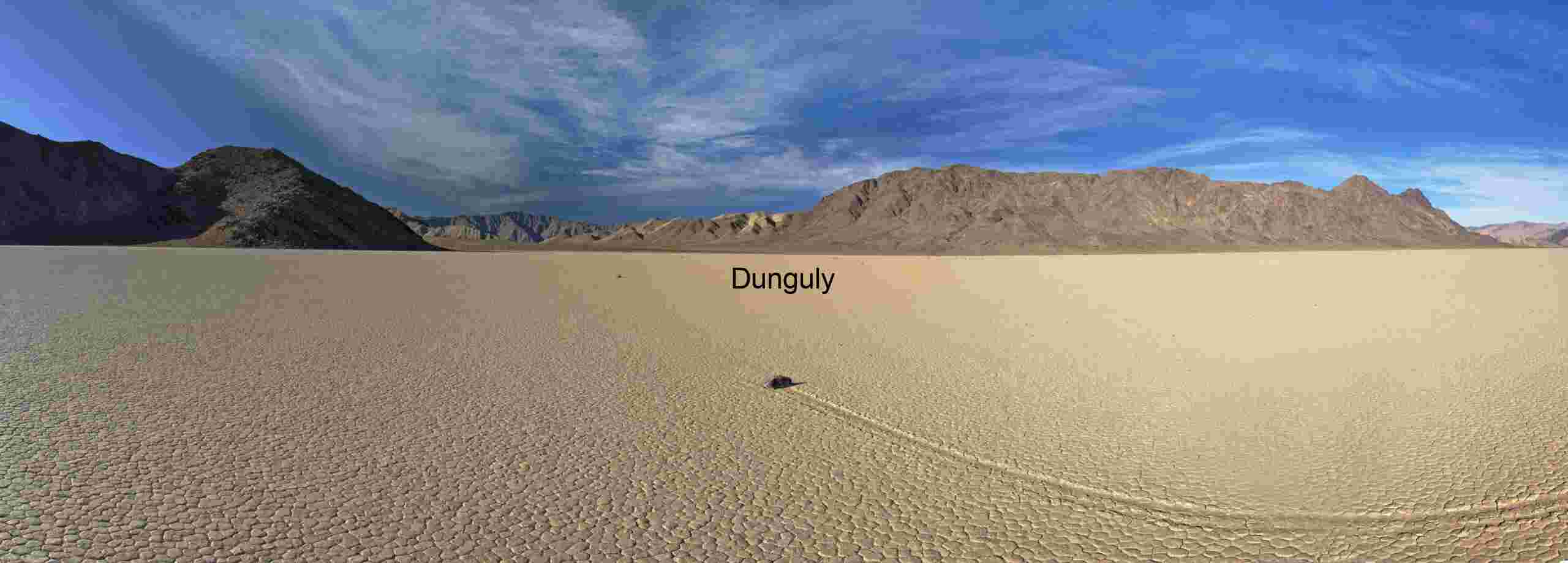 Solitary rock glides across the flat playa, carving a natural mystery path under a partly cloudy sky.